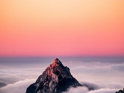 An aerial view of a mountain covered in fog under the beautiful pink sky