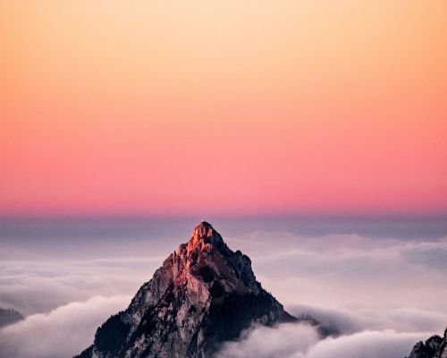 An aerial view of a mountain covered in fog under the beautiful pink sky